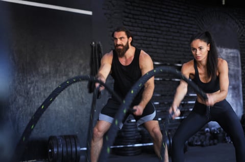 Athletic young couple with battle rope doing exercise in functional training fitness gym