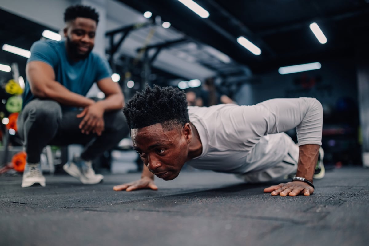 Young muscular athlete performing push-ups while receiving guidance from a personal trainer in a modern gym setting