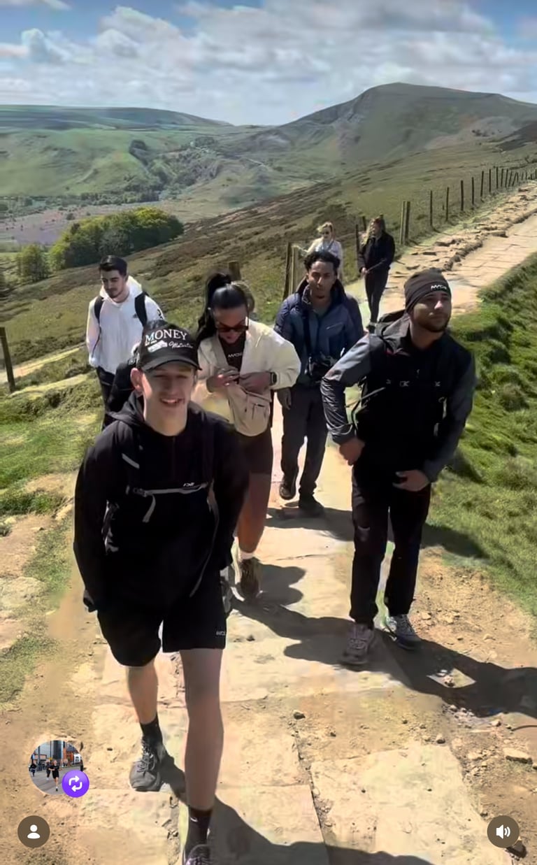 Group of hikers walking on a dirt trail through rolling green hills and moorland with mountains in the background
