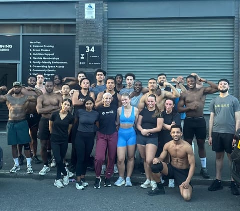 Group of diverse fitness enthusiasts posing together outside a gym facility with a blue metal garage door